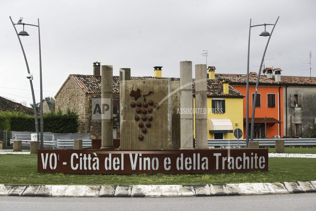 Luca Bruno Writing reading in Italian 'Vo - Town of wine and trachyte'' embraces a sculpture on a round-a-bout in town of Vo Euganeo, northern Italy, Wednesday, Feb. 10, 2021. Shockwaves ran through the wine-making village of Vo, west of Venice, as word spread last Feb. 21 that a retired roofer had died of the new coronavirus becoming the first known COVID-19 victim in the West. (AP Photo/Luca Bruno)