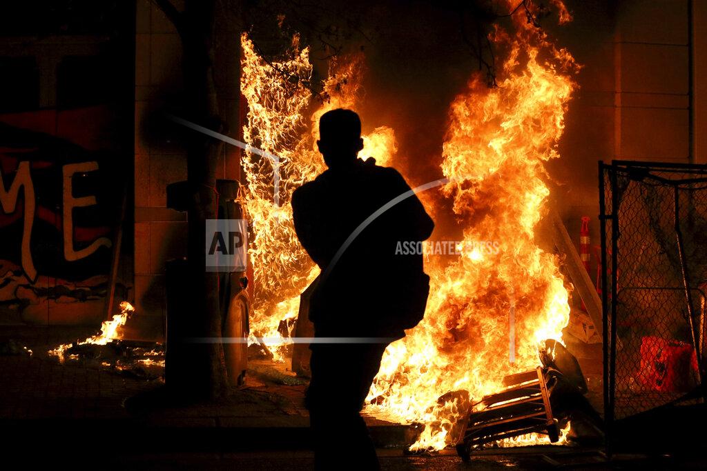 Dave Killen Protesters lit a portable bathroom on fire in downtown Portland, Ore., Friday, April 16, 2021. Police in Portland, Oregon, said Saturday they arrested four people after declaring a riot Friday night when protesters smashed windows, burglarized businesses and set multiple fires during demonstrations that started after police fatally shot a man while responding to reports of a person with a gun. (Dave Killen/The Oregonian via AP)