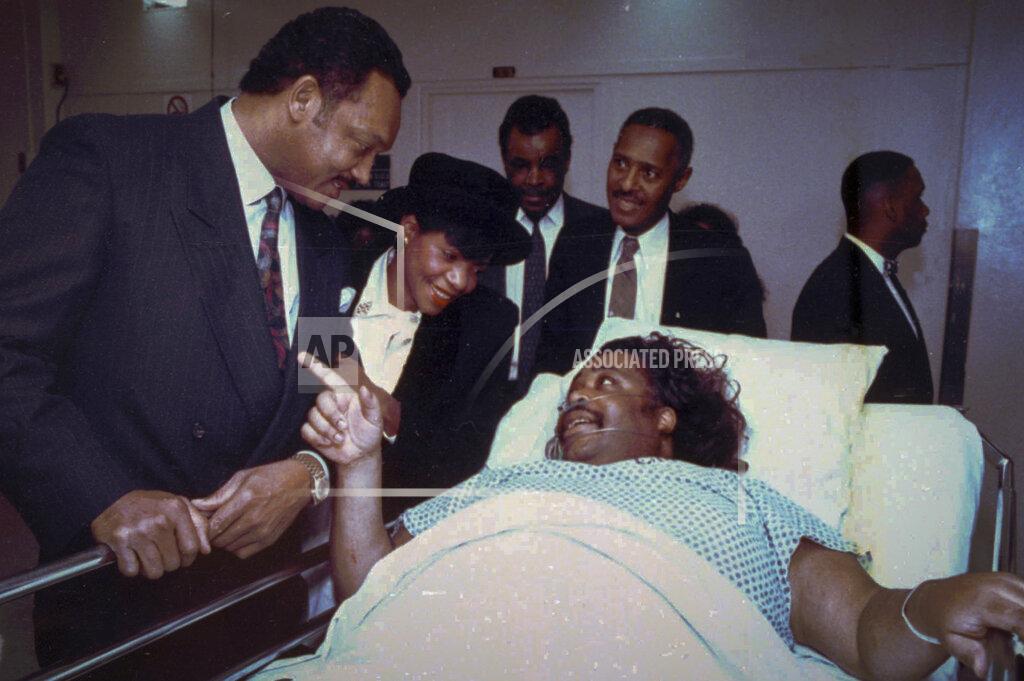 Chester Higgins Jr. FILE - In this Jan. 13, 1991, file photo, the Rev. Jesse Jackson, left, singer Melba Moore, second from left, union leader Jim Bell, center, and the Rev. Herbert Daughtry, second from right, visiting with the Rev. Al Sharpton in a New York hospital, recovering from a knife attack a day earlier as he prepared to lead protest in the Bensonhurst area of the Brooklyn borough of New York, where Black teenager Yusuf Hawkins was fatally shot. For more than three decades, Sharpton, 65, has been a go-to advocate for Black American families seeking justice and peace in the wake of violence and countless incidents that highlight systemic racism. (Chester Higgins Jr./The New York Times via AP, Pool, File)
