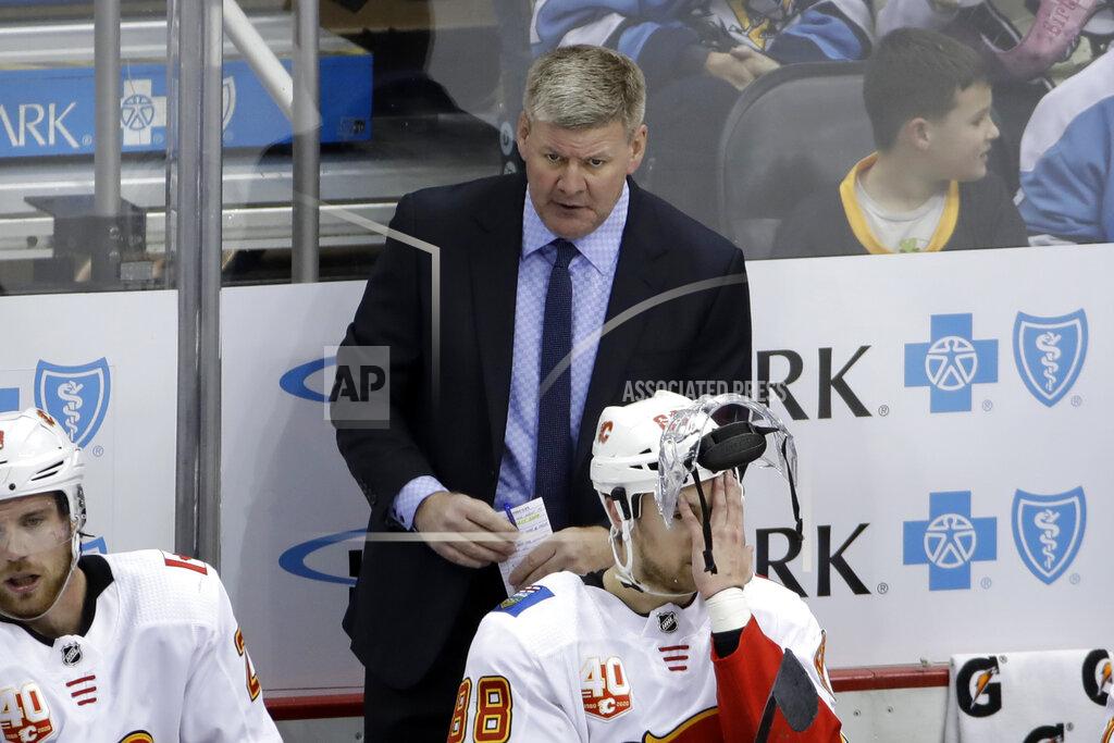 Gene J. Puskar Calgary Flames head coach Bill Peters stands behind Andrew Mangiapane (88) during the third period of an NHL hockey game against the Pittsburgh Penguins in Pittsburgh, Monday, Nov. 25, 2019. The Penguins won in overtime 3-2. (AP Photo/Gene J. Puskar)