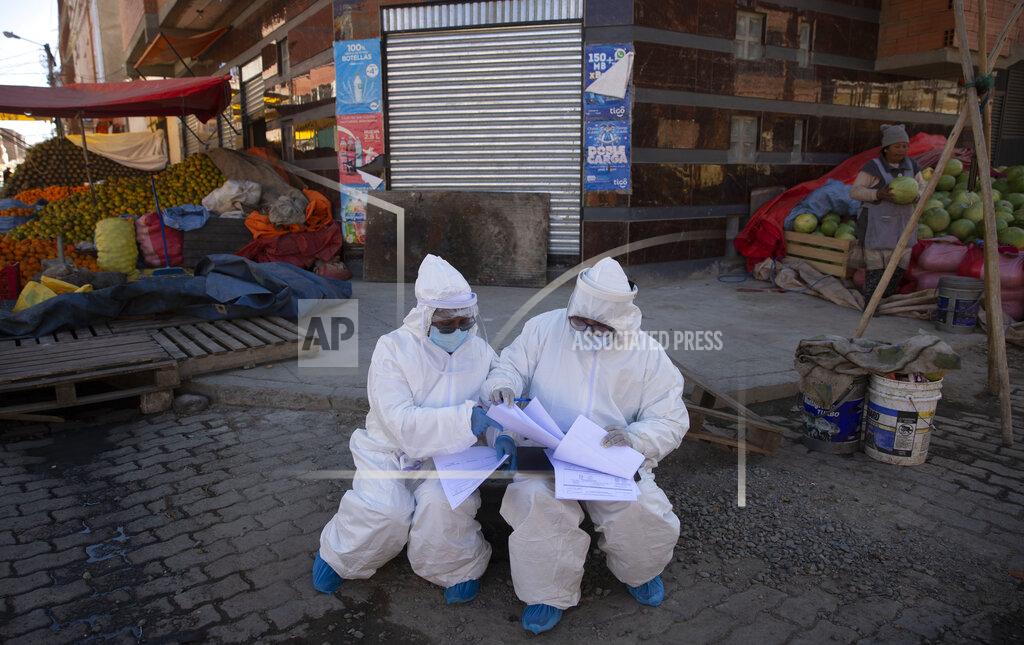 Juan Karita Healthcare workers dressed in full protective gear organize their documents of data they have collected during a house-to-house new coronavirus testing drive, ringed by a produce market in the Villa Dolores neighborhood of El Alto, Bolivia, Saturday, July 18, 2020. (AP Photo/Juan Karita)