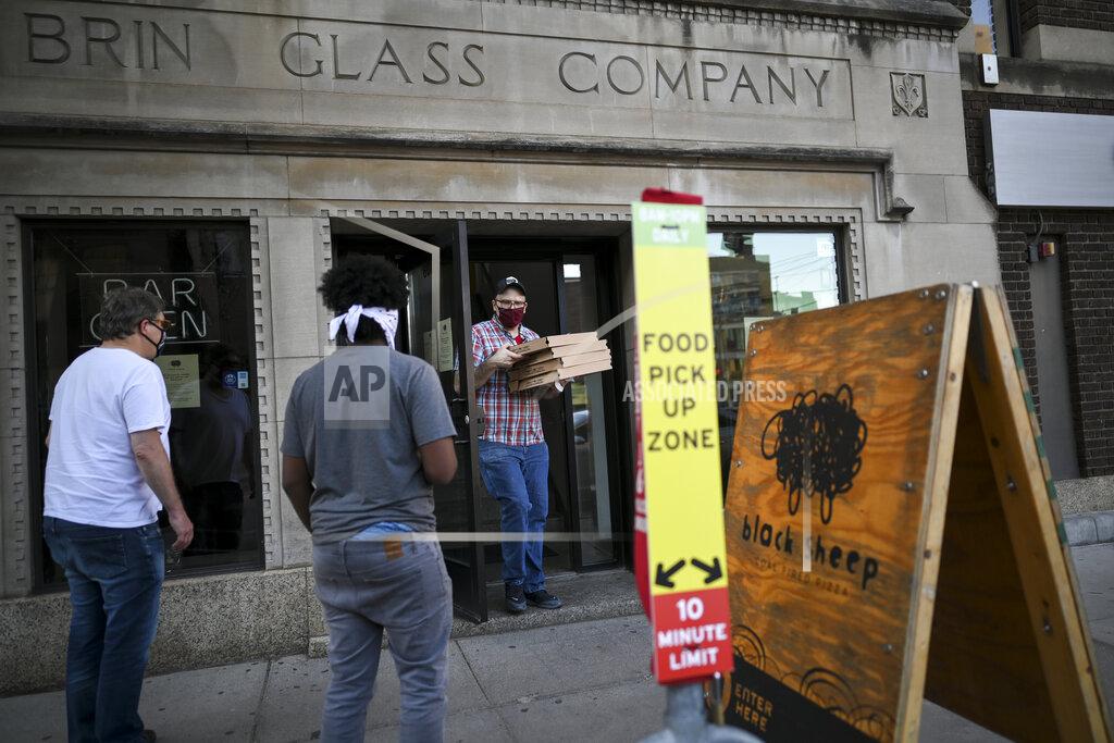 Aaron Lavinsky Andrew Schmittfrenz, a manager at Black Sheep's North Loop location, walks outside to deliver a few orders of pizza to customers waiting for their takeout orders amid the coronavirus pandemic, Wednesday, May 20, 2020, in Minneapolis. (Aaron Lavinsky/Star Tribune via AP)