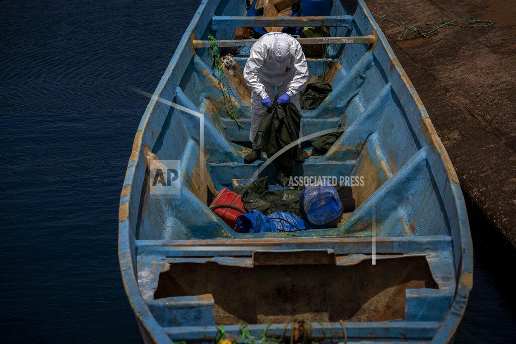 Emilio Morenatti A police officer inspects a boat where 15 Malians were found dead adrift in the Atlantic on Thursday, Aug. 20, 2020 in Gran Canaria island, Spain. The 15 lifeless men were spotted inside a boat on Aug. 19 by a Spanish plane 80 nautical miles (148 kilometers, 92 miles) from the island of Gran Canaria. Police collected what was left behind as evidence: a wallet, a dozen cell phones, windbreakers and galoshes. (AP Photo/Emilio Morenatti)