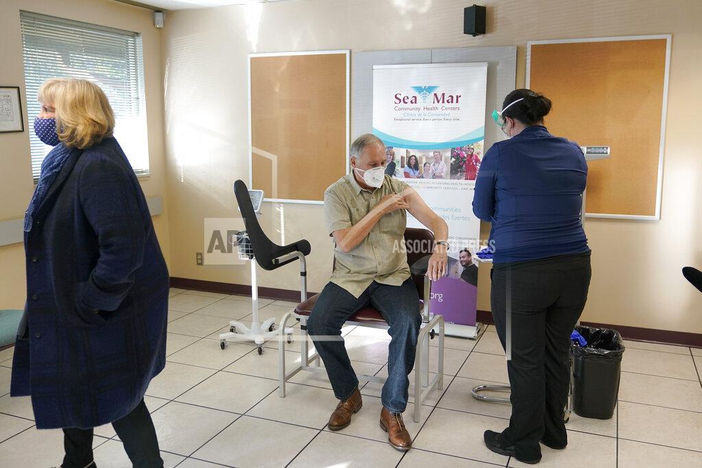 Ted S. Warren Washington Gov. Jay Inslee, center, rolls up his sleeve as his wife Trudi right, stands nearby he prepares to be given the first shot of the Moderna COVID-19 vaccine, Friday, Jan. 22, 2021, by medical assistant Elizabeth Smalley, right, at a Sea-Mar Community Health Center in Olympia, Wash. (AP Photo/Ted S. Warren)