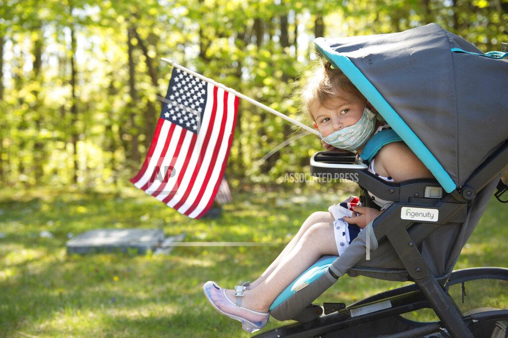 Daryn Slover Anna Wines, 3, of Bath, Maine, helps carry American flags while her family places new flags next to the gravestone of each veteran at Riverside Cemetery in Lewiston, Maine, Thursday, May 21, 2020. Volunteers will place nearly 7,500 new flags near veterans' graves at the 13 cemeteries across Lewiston, Maine, by Memorial Day. (Daryn Slover/Sun Journal via AP)