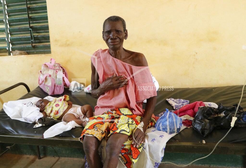 Sam Mednick A woman sits on a bed in a small clinic in Zeguedessin village on the outskirts of Burkina Faso's capital, Ouagadougou, receiving medical treatment on Thursday Oct. 8, 2020. The hospital's solar fridge has been broken for a year meaning there is less space in the hospital to store large amounts of vaccines. The vaccine cold chain hurdle is just the latest disparity of the pandemic weighted against the poor, who more often live and work in crowded conditions that allow the virus to spread, have little access to medical oxygen vital to COVID-19 treatment, and whose health systems lack labs, supplies or technicians to carry out large-scale testing. (AP Photo/Sam Mednick)