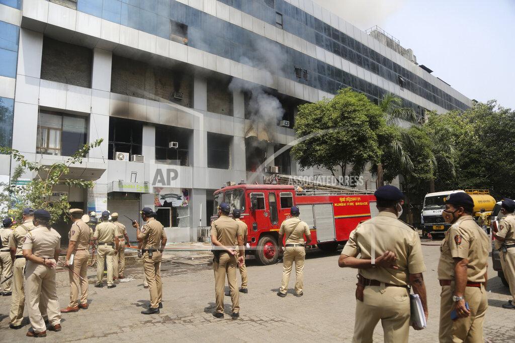 Police officers stand by as firefighters work to control a fire at a Sunrise Hospital, a private hospital treating coronavirus patients, in India's financial capital of Mumbai, Friday, March 26, 2021. The fire killed at least 10 people and more than 70 patients were evacuated to other hospitals in the city. Firefighting crews were still working to control the blaze, which broke out early Friday, with 20 fire engines and ambulances at the scene, said an official at the fire services control room. (AP Photo/Emmanual Yogini)