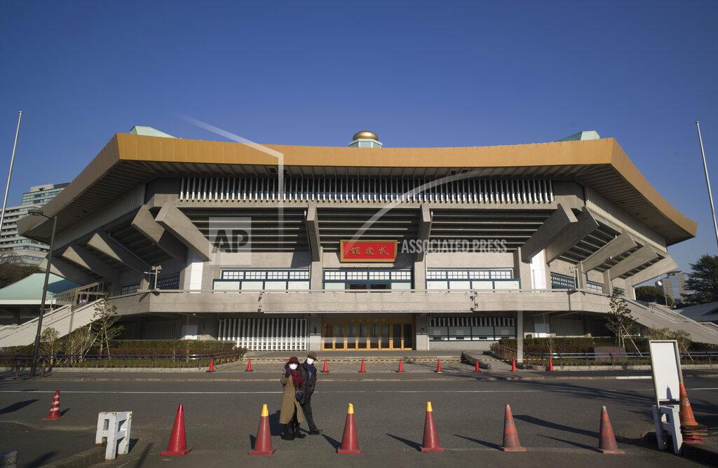 A man and a woman walk past the Nippon Budokan arena, one of the venues planned to be used in the rescheduled Tokyo Olympics, in Tokyo on Thursday, Jan. 21, 2021. The postponed Tokyo Olympics are to open in just six months. Local organizers and the International Olympic Committee say they will go ahead on July 23. But it’s still unclear how this will happen with virus cases surging in Tokyo and elsewhere around the globe. (AP Photo/Hiro Komae)