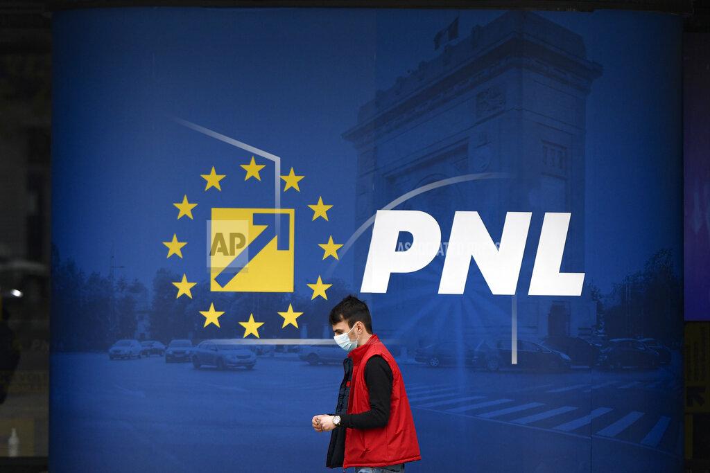 Andreea Alexandru A man wearing a mask for protection against the COVID-19 infection walks by the logo of the Liberal Party in Bucharest, Romania, Thursday, Dec. 3, 2020. Romania will hold parliamentary elections on Sunday Dec. 6. (AP Photo/Andreea Alexandru)