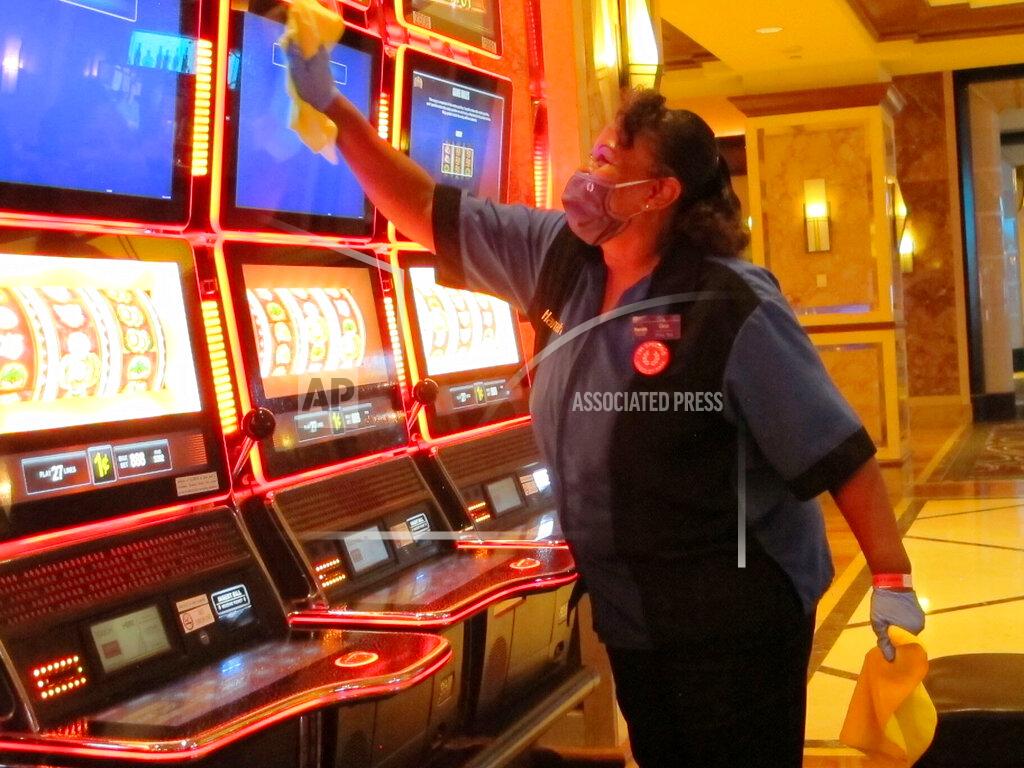 Wayne Parry In this July 1, 2020 photo, Jeorganna Barnes, a worker at Harrah's casino in Atlantic City, N.J., wipes slot machines with disinfectant as the casino prepared to reopen after 3 1/2 months of being shut down due to the coronavirus. On Nov. 23, 2020, New Jersey gambling regulators released figures showing Atlantic City's casinos saw their gross operating profits decline by 37% in the third quarter of 2020 as they reopened under restrictions designed to slow the spread of the virus. (AP Photo/Wayne Parry)