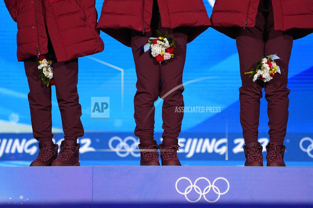Jae C. Hong Canadian athletes hold their bouquets between their legs to wear their face masks during the medal ceremony for the men's 5000-meters relay short track speedskating at the 2022 Winter Olympics, Thursday, Feb. 17, 2022, in Beijing. (AP Photo/Jae C. Hong)
