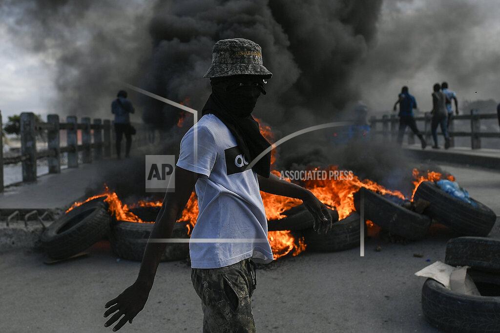 Matias Delacroix A protester demanding justice for the assassinated President Jovenel Moise stands near a burning barricade in Cap-Haitien, Haiti, Thursday, July 22, 2021. Demonstrations after a memorial service for Moise turned violent on Thursday afternoon with protesters shooting into the air, throwing rocks and overturning heavy concrete barricades next to the seashore as businesses closed and people took cover. (AP Photo/Matias Delacroix)
