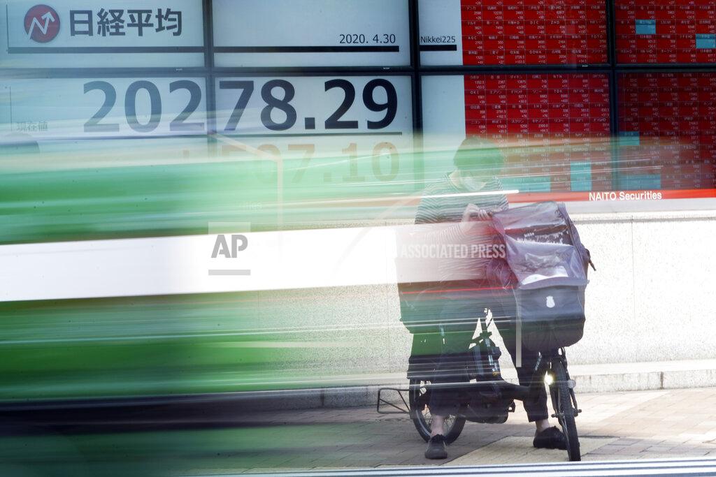 A man rides a bicycle in front of an electronic stock board showing Japan's Nikkei 225 index at a securities firm in Tokyo Thursday, April 30, 2020. Asian shares advanced on Thursday, riding a wave of optimism about a possible treatment for the coronavirus that set off a rally on Wall Street powerful enough to override data showing the U.S. economy had logged its worst quarterly performance since 2009. (AP Photo/Eugene Hoshiko)