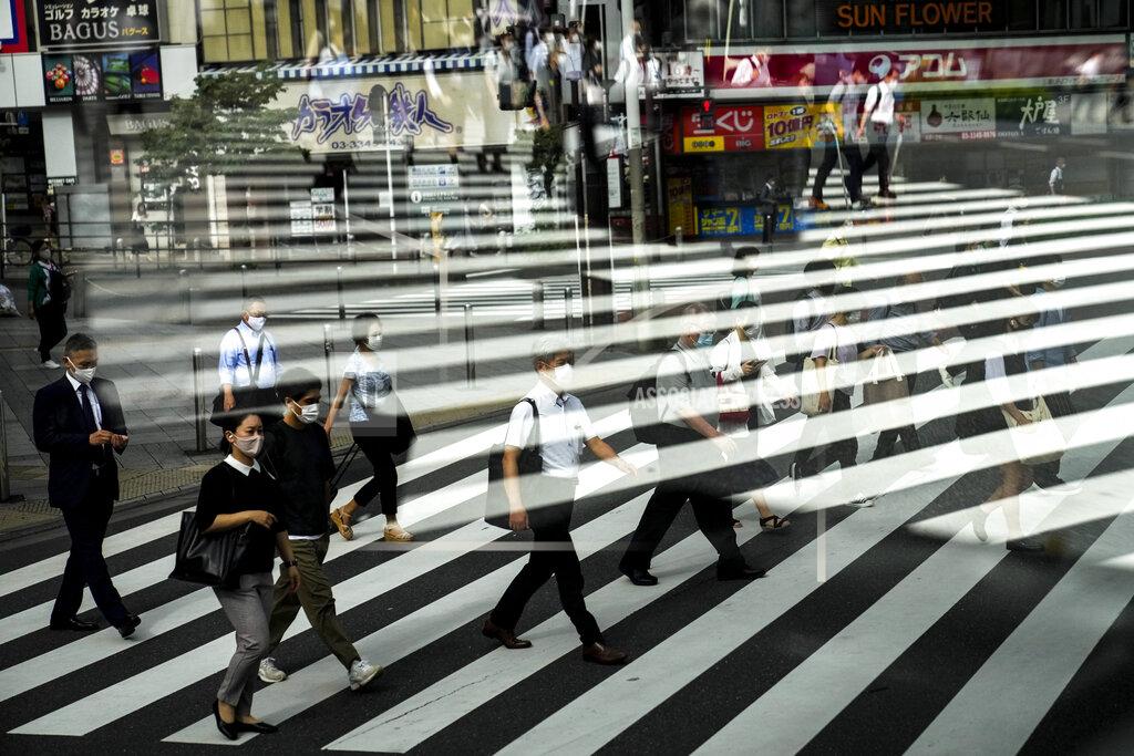 Jae C. Hong Commuters are reflected in a bus window as they cross the street Thursday, July 15, 2021, in Tokyo. The pandemic-delayed 2020 Summer Olympics open on July 23 without spectators at most venues. (AP Photo/Jae C. Hong)
