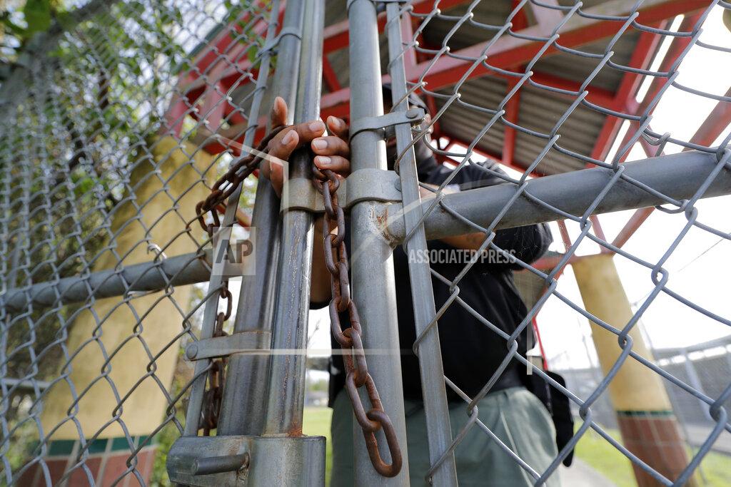 Gerald Herbert FILE - In this March 13, 2020 file photo, School Resource Officer Donald Lee locks the gates of the Dr. Martin Luther King, Jr. Elementary School for Science and Technology, after all the students left, in New Orleans. Where political divides marred early recovery efforts after Hurricane Katrina in 2005, Louisiana is showing rare political unity in the fight against the new coronavirus. (AP Photo/Gerald Herbert, File)