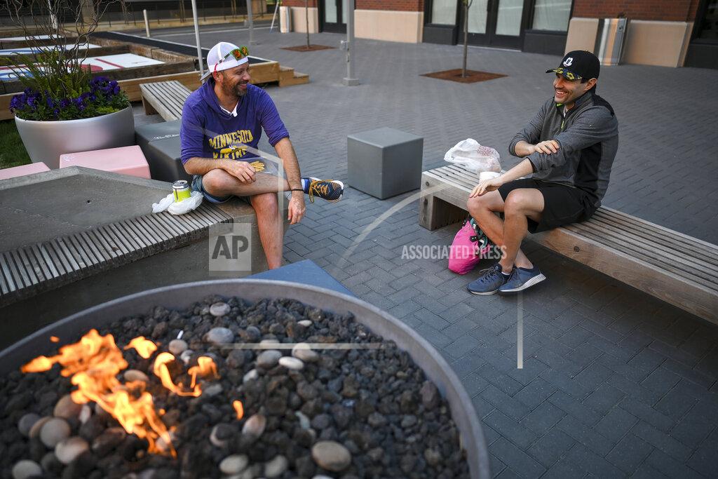 Aaron Lavinsky Friends Jon Feustel, left, and Mark Siebenaller, from the North Loop, drink beer and eat pizza from The Freehouse in the courtyard outside the brewpub, Wednesday, May 20, 2020, in Minneapolis, as the two diners eat their takeout orders outside the restaurant amid the coronavirus pandemic. (Aaron Lavinsky/Star Tribune via AP)