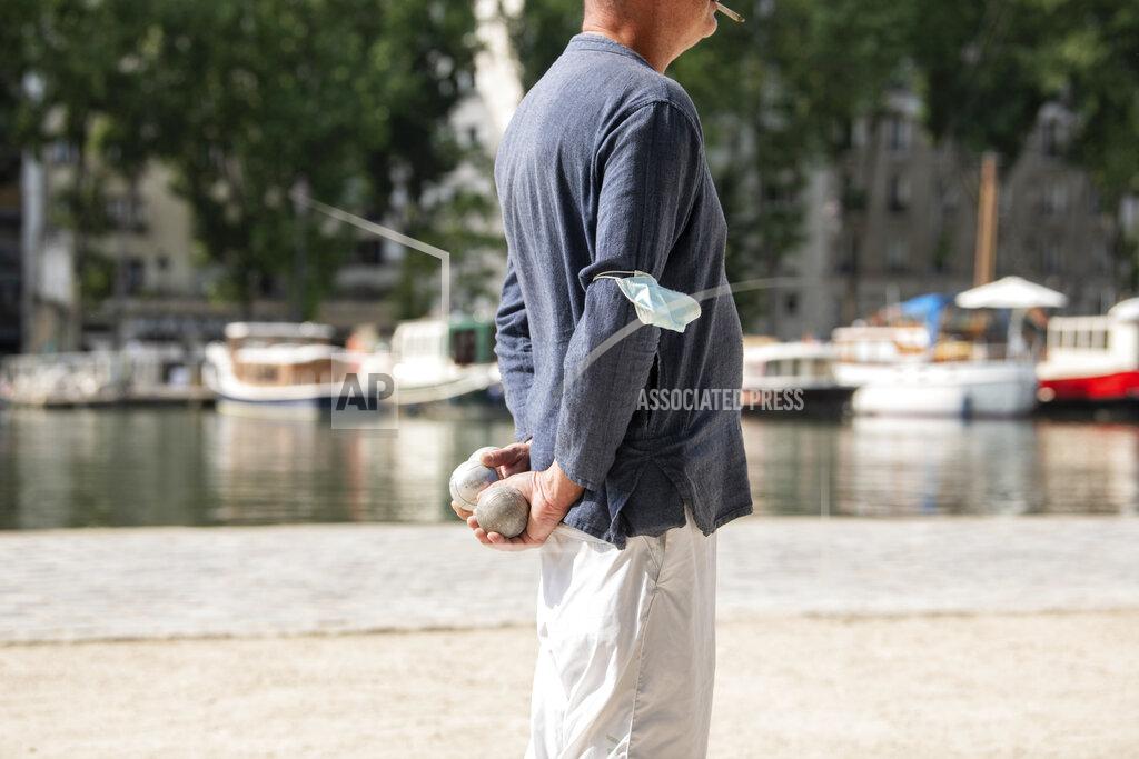 Benjamin Girette A man plays pétanque with his mask attached to his arm Wednesday, June 16, 2021 along the Canal de l'Ourcq in Paris. France on Wednesday eased several COVID-19 restrictions, with authorities saying it's no longer always mandatory to wear masks outdoors, and halting an 8-month nightly coronavirus curfew this weekend. (AP Photo/Benjamin Girette)