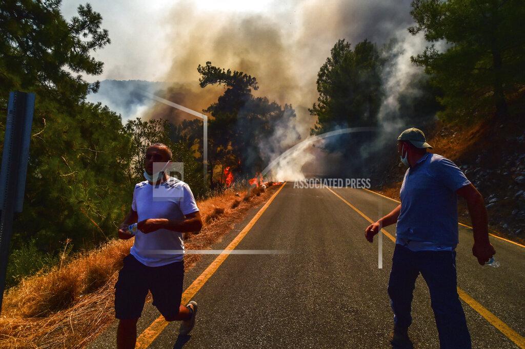 Ismail Coskun People run away as the wildfires engulf an area near the seashore, forcing people to be evacuated by boats, in Bodrum, Mugla, Turkey, Sunday, Aug. 1, 2021. Wildfires in the Turkish holiday destinations of Antalya and Mugla are still raging as firefighters worked to battle the blazes for a fifth day. Authorities warned tourists and residents to keep evacuating Turunc, a town in the seaside resort of Marmaris, and navy ships waited in the sea there to see if a bigger evacuation was needed. (Ismail Coskun/IHA via AP)