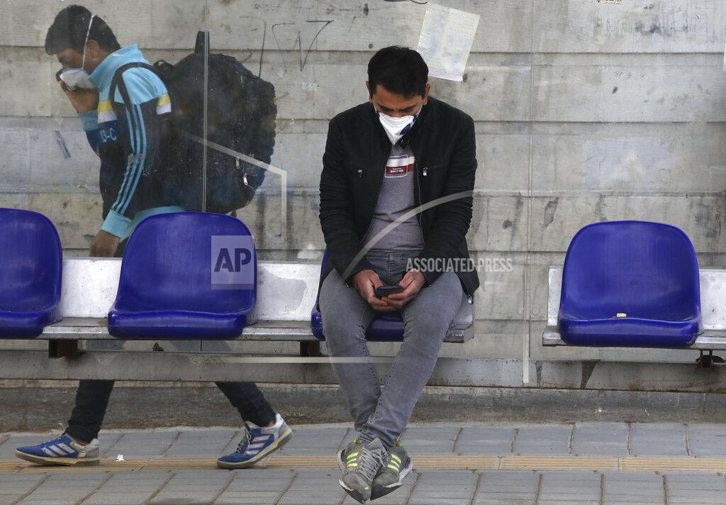 Vahid Salemi A man wearing a face mask to curb the spread of the new coronavirus sits at a bus stop, as another man walks past, in Niavaran in northern Tehran, Iran, Thursday, April 16, 2020. Authorities have canceled ceremonies marking the anniversary of the death of Ayatollah Khomeini, the founder of the Islamic Republic over COVID-19 disease concerns, which underscored Iranian officials' expectation that the virus crisis will continue for several more weeks. (AP Photo/Vahid Salemi)