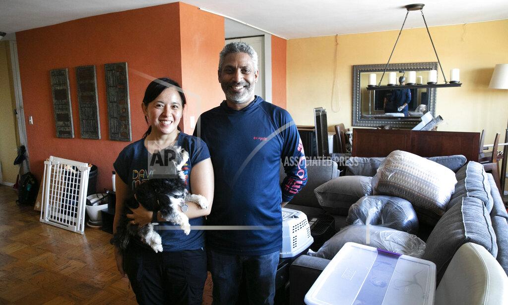 Joyce and Anil Lilly pose in their living room with their dog Max as they move out of their Bronx apartment, Tuesday, July 21, 2020, in New York. If the outbreak roars back in the city, they will not be sheltering again in the apartment. They just bought a house an hour north in the Hudson Valley. (AP Photo/Mark Lennihan)