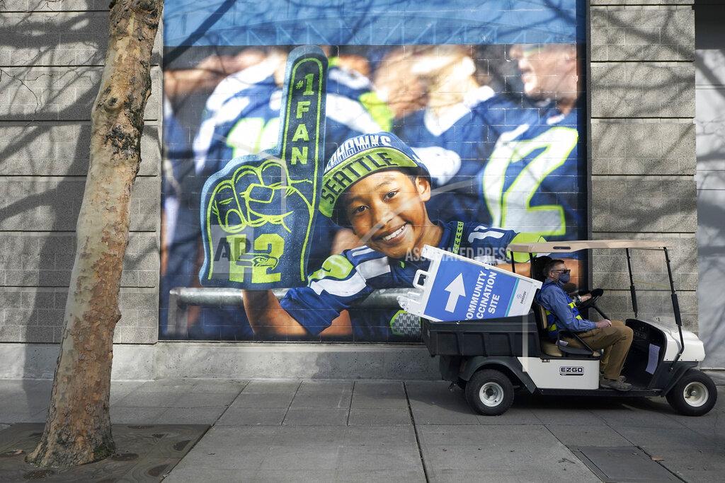 Ted S. Warren FILE - A cart carries a sign that reads "Community Vaccination Site," past a photo of a Seattle Seahawks fan, on the first day of operation of a mass COVID-19 vaccination site at the Lumen Field Events Center in Seattle, which adjoins the field where the NFL football Seahawks and the MLS soccer Seattle Sounders play their games, in this Saturday, March 13, 2021, file photo. All 32 teams are conducting open practices on Saturday, July 31, as part of "Back Together Saturday." Some teams will be offering COVID-19 vaccinations at their facilities. (AP Photo/Ted S. Warren, File)