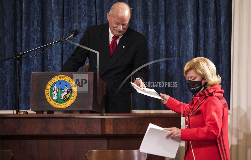 Mark Delk, president of the Electoral College, hands president teller Susan Mills electoral ballots to be shared with electors in the house chambers of the Old State Capitol building in Raleigh, N.C., on Monday, Dec. 14, 2020. (Julia Wall/The News & Observer via AP)