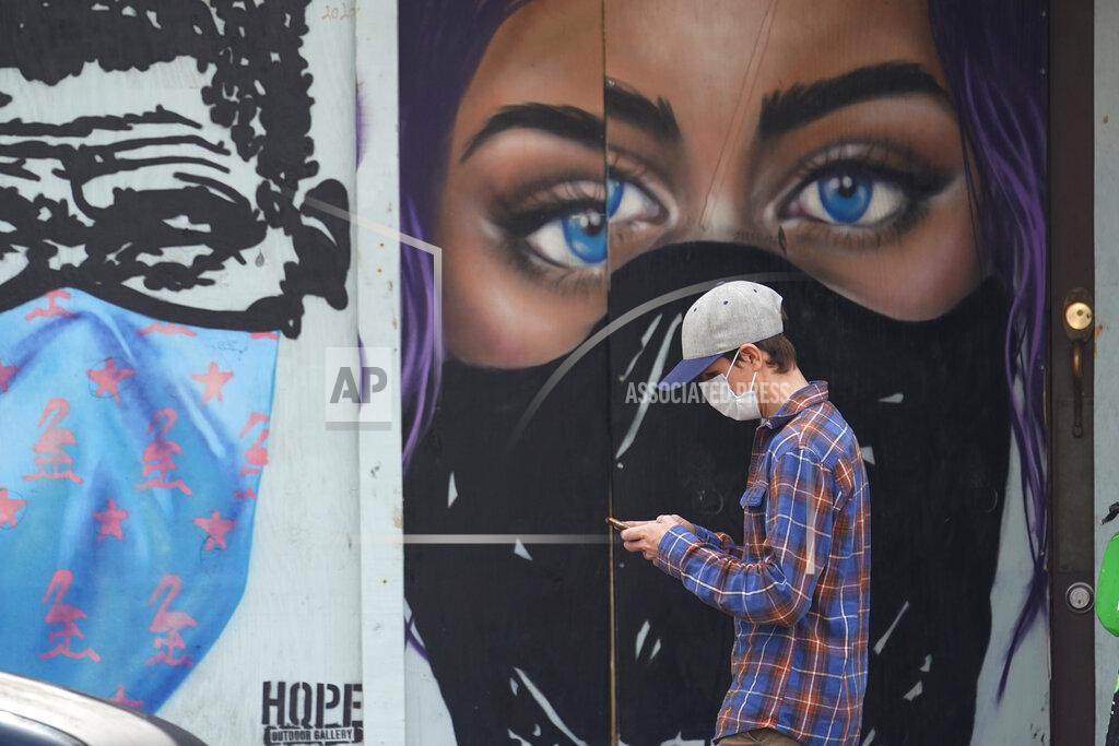 Eric Gay A pedestrian wearing a mask to protect against the spread on COVID-19 passes murals painted on a boarded-up business in downtown Austin, Texas, Tuesday, March 9, 2021. Texas Gov. Greg Abbot's mask mandate for the state ends Wednesday. (AP Photo/Eric Gay)