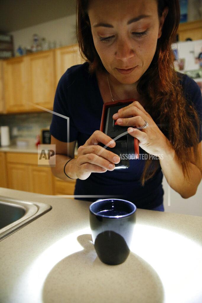Caleb Jones Lauren Wright, a Navy spouse whose family was sickened by jet fuel in their tap water, looks at a water sample from her kitchen sink at her home in Honolulu, Friday, July 1, 2022. A Navy investigation says shoddy management and human error caused fuel to leak into Pearl Harbor's tap water last year. The leak poisoned thousands of people and forced military families to evacuate their homes for hotels. (AP Photo/Caleb Jones)