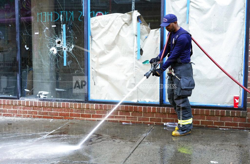 Michael Perez ADDS CONTEXT AND DETAIL THAT THESE BULLET HOLES ARE FROM A PRIOR SHOOTING - A Philadelphia fireman washes blood off the sidewalk at the scene of a fatal overnight shooting on South Street in Philadelphia, Sunday, June 5, 2022, where bullet holes on a storefront window from a prior shooting can also be seen. (AP Photo/Michael Perez)