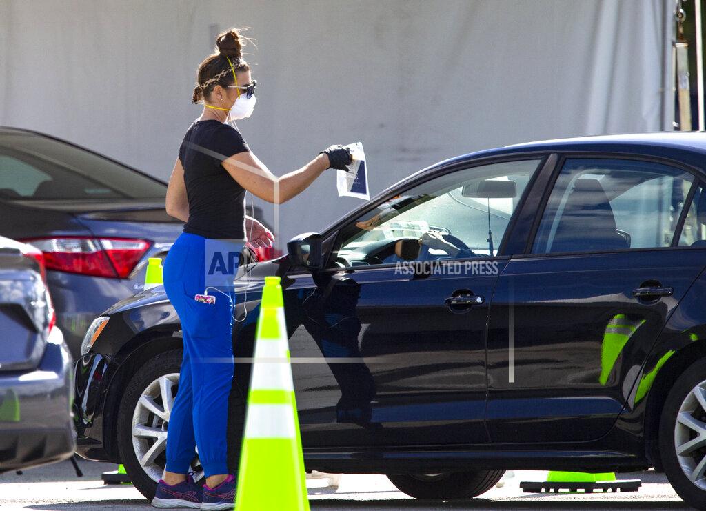 David Santiago A health care worker direct a person to use a swab for a self administered test at the Miami-Dade County Youth Fairgrounds at Tamiami Park, on Sunday, Nov. 29, 2020 in Miami. (David Santiago/Miami Herald via AP)