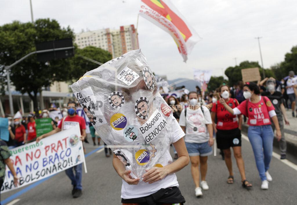 Bruna Prado A woman wears a plastic bag decorated with stickers depicting Brazilian President Jair Bolsonaro as a virus, during a demonstration against Bolsonaro's handling of the coronavirus pandemic and economic policies protesters say harm the interests of the poor and working class, in Rio de Janeiro, Brazil, Saturday, June 19, 2021. Brazil is approaching an official COVID-19 death toll of 500,000 — second-highest in the world. (AP Photo/Bruna Prado)