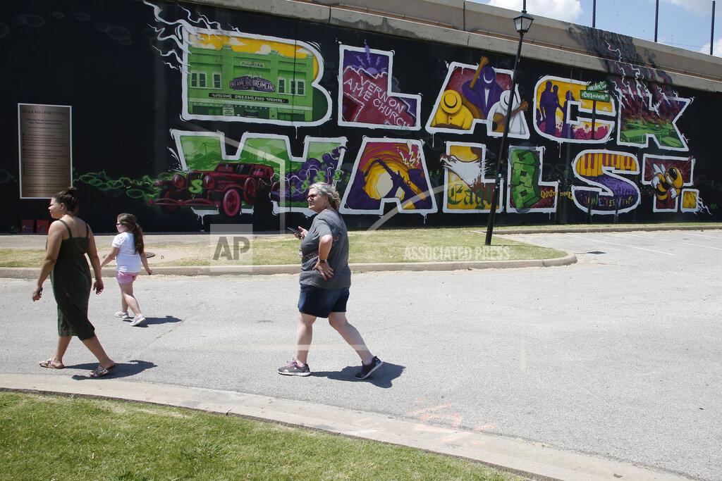Sue Ogrocki People walk past a Black Wall Street mural in the Greenwood district in Tulsa, Okla., Monday, June 15, 2020. Despite the Oklahoma heat, visitors of all races come to the site of the destroyed black community on this morning. (AP Photo/Sue Ogrocki)