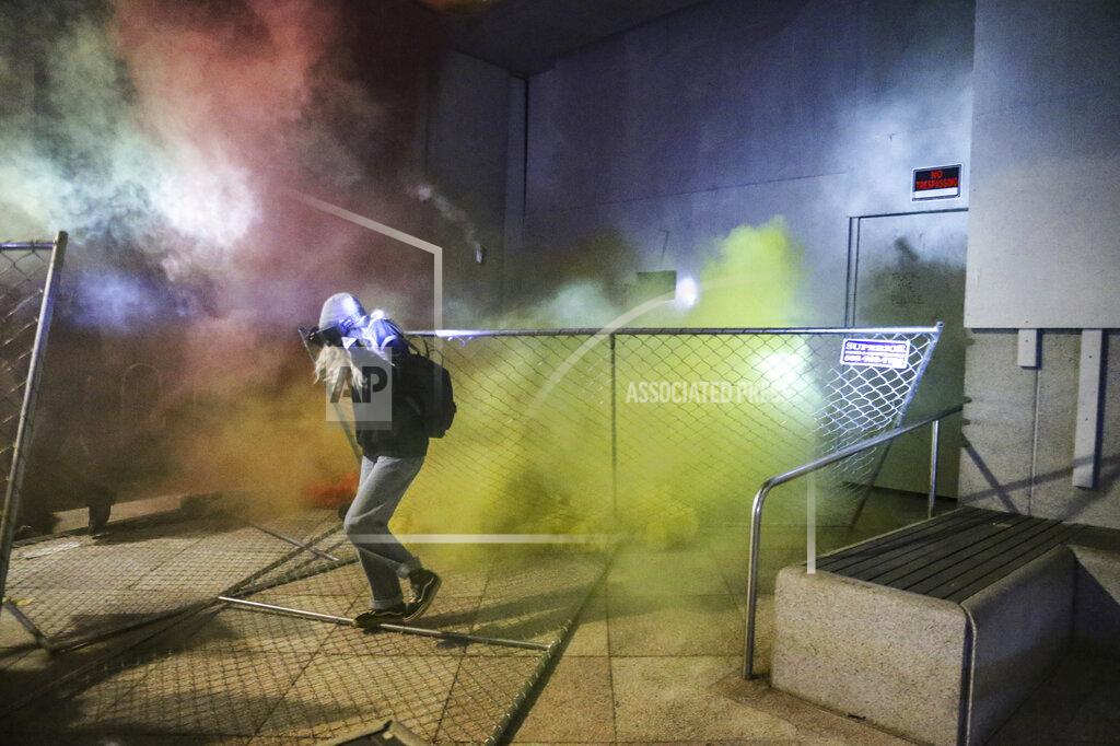 Dave Killen A protesters runs as police respond during a demonstration, Friday, July 17, 2020 in Portland, Ore. Militarized federal agents deployed by the president to Portland, Oregon, fired tear gas against protesters again overnight as the city’s mayor demanded that the agents be removed and as the state’s attorney general vowed to seek a restraining order against them. (Dave Killen/The Oregonian via AP)