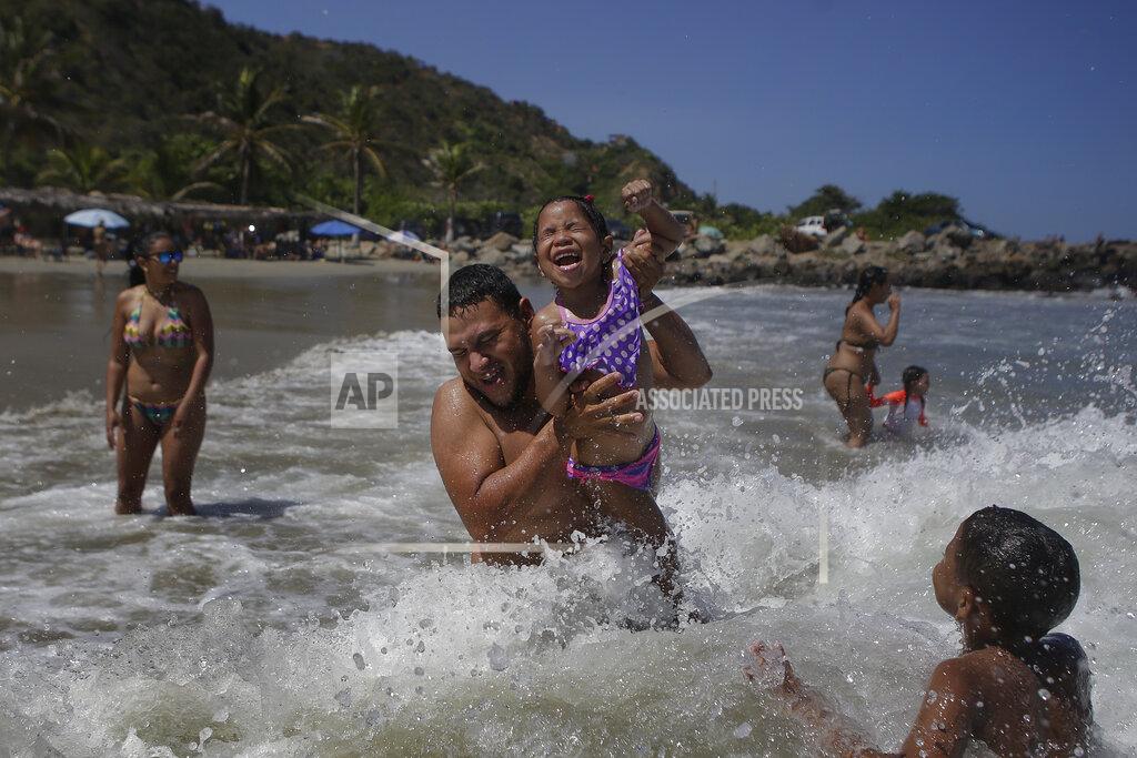 Matias Delacroix Caracas resident Jose Velasco lifts his daughter Ashley Velasco above a wave off La Ultima beach after it recently reopened following a lockdown to contain the spread of COVID-19 in La Guaira, Venezuela, Friday, Oct. 23, 2020. Strict quarantine restrictions forced the closure of beaches across the country in March and reopened this week. (AP Photo/Matias Delacroix)