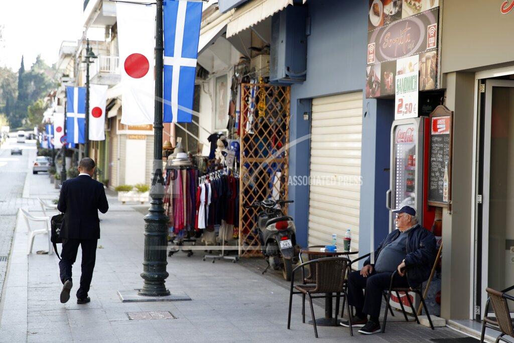 Thanassis Stavrakis A local resident sits at a cafe as a Japanese official walks in the town of Olympia, southern Greece, Wednesday, March 11, 2020. Greek Olympic officials in ancient Olympia, birthplace of the ancient Olympics are holding a pared-down flame-lighting ceremony for the Tokyo Games due to concerns over the spread of the coronavirus. Both Wednesday's dress rehearsal and Thursday's lighting ceremony will be closed to the public, while organizers have slashed the number of officials from the International Olympic Committee and the Tokyo Organizing Committee, as well as journalists at the flame-lighting. (AP Photo/Thanassis Stavrakis)