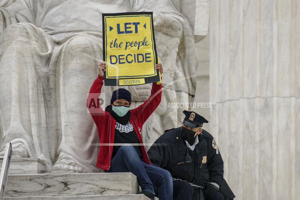 J. Scott Applewhite A protester opposed to the Senate's race to confirm Amy Coney Barrett is removed by police after chaining themselves to a railing and holding a sign while sitting atop the statue Contemplation of Justice, at the Supreme Court building in Washington, Sunday, Oct. 25, 2020. (AP Photo/J. Scott Applewhite)