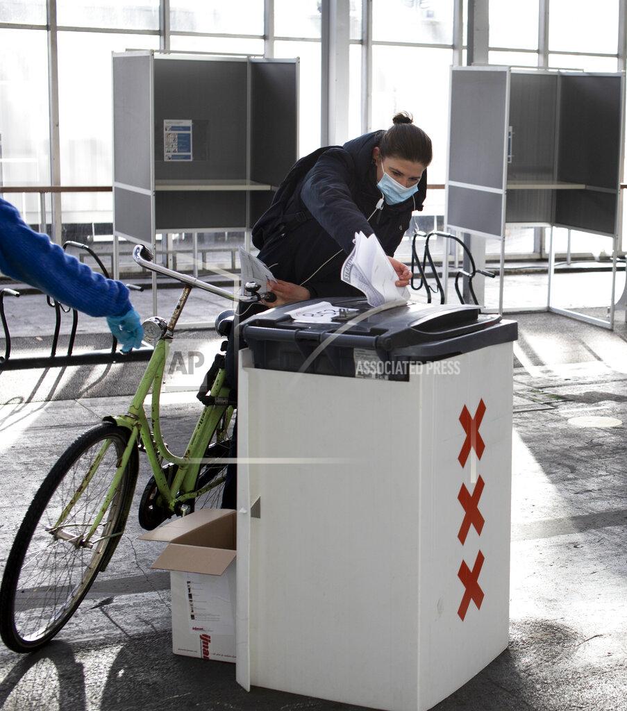 Peter Dejong A woman casts her ballot in ride through polling station for bicycles in Amsterdam, Netherlands, Monday, March 15, 2021. Polling stations opened across the Netherlands early Monday in a general election that has been spread over three days to allow people to vote safely during the coronavirus pandemic. (AP Photo/Peter Dejong)