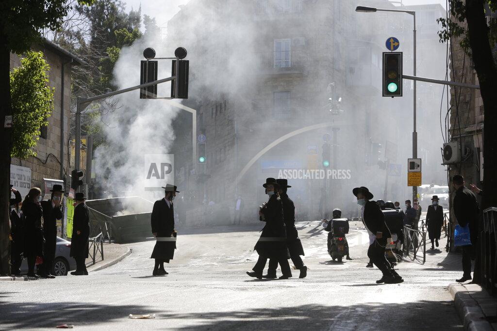 Men walk amid smoke from a dumpster fire, in an ultra-Orthodox neighborhood in Jerusalem, Sunday, Jan. 24, 2021. Ultra-Orthodox demonstrators clashed with Israeli police officers dispatched to close schools in Jerusalem and Ashdod that had opened in violation of health regulations on Sunday. (AP Photo/Sebastian Scheiner)