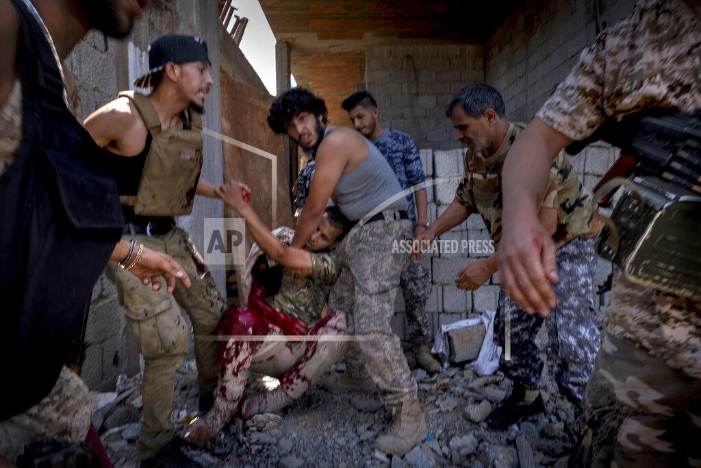 FILE - In this Sept. 7, 2019 file photo, a mortally wounded fighter of the 'Shelba' unit, allied with the U.N.-supported Libyan government, is moved by comrades after being shot at the Salah-addin neighborhood front line in Tripoli, Libya. The head of Libya’s internationally recognized government Tuesday, May 5, 2020, called for a renewal of U.N.-brokered talks to end divisions in the oil-rich country, amid escalating military clashes and increasing tensions between the main players in the capital Tripoli. (AP Photo/Ricard Garcia Vilanova, File)