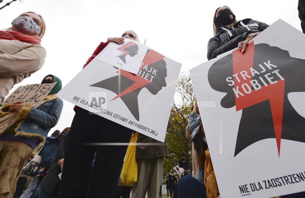 Women's rights activists with posters of the Women's Strike action protest against recent tightening of Poland's restrictive abortion law in front of the parliament building as inside, guards had to be used to shield right-wing ruling party leader Jaroslaw Kaczynski from angry opposition lawmakers, in Warsaw, Poland, on Tuesday, Oct. 27, 2020. Massive nationwide protests have been held ever since a top court ruled Thursday that abortions due to fetal congenital defects are unconstitutional. Slogan reads 'Women’s Strike'. (AP Photo/Czarek Sokolowski)