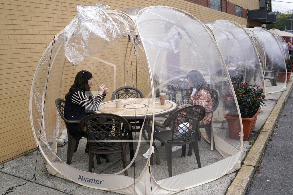 Seth Wenig Aviva Markowitz, left, and Rivka Alter enjoy a drink in a protective bubble at the Lazy Bean Cafe in Teaneck, N.J., Thursday, Oct. 22, 2020. The bubbles have been popular with customers, both for social distancing and warmth as the weather turns colder. New Jersey's climbing number of COVID-19 cases are beginning to spread to northern counties around New York, Gov. Phil Murphy said Thursday. Essex, Union, Hudson and Bergen counties reported more than 100 new cases overnight, Murphy said, eclipsing recent hot spots in Ocean and Monmouth counties. (AP Photo/Seth Wenig)