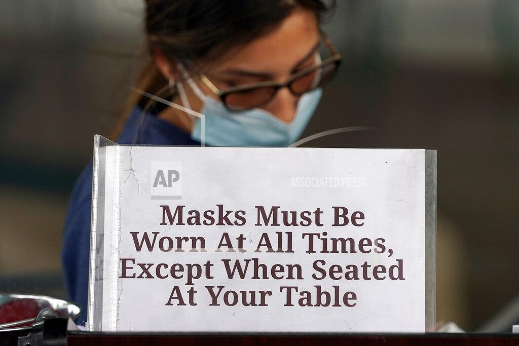 David J. Phillip Hostess Carla Alexander waits behind a sign that ask customers to wear masks at the Saint Arnold Brewing Company, Friday, June 26, 2020, in Houston. Texas Gov. Greg Abbott announced Friday that he is shutting bars back down and scaling back restaurant capacity to 50%, in response to the increasing number of COVID-19 cases in Texas. (AP Photo/David J. Phillip)