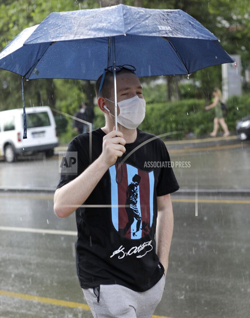 A man wearing a face mask to protect against the spread of coronavirus, walks in rain in a popular street, in Ankara, Turkey, Wednesday, June 17, 2020. Turkey has made the wearing of face masks mandatory in five more provinces, following an uptick in COVID-19 cases. Health Minister Fahrettin Koca tweeted Tuesday that the wearing of masks is now compulsory in 42 of Turkey's 81 provinces.(AP Photo/Burhan Ozbilici)