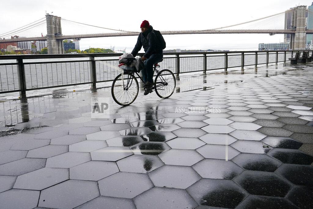 Mary Altaffer A cyclist is framed by the Brooklyn Bridge as he rides during a break in the heavy rain, Tuesday, Oct. 26, 2021, in New York. A flash flood watch is in effect as a nor'easter moves through the New York metro area. (AP Photo/Mary Altaffer)