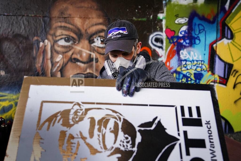 Brynn Anderson Artist Brandon Litman paints a U.S. Senator-elect Raphael Warnock, D-Ga., campaign poster for voters waiting in line after Georgia's Senate runoff race on Sunday, Jan. 10, 2021, in Atlanta. (AP Photo/Brynn Anderson)