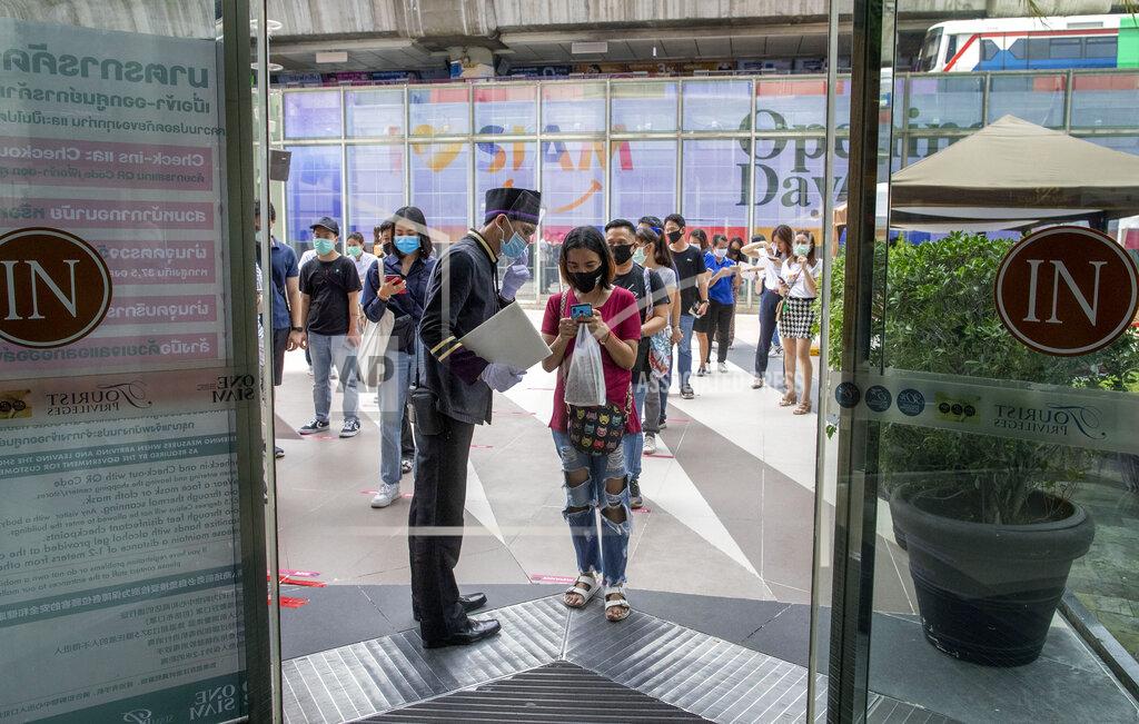 A woman displays her phone to doorman, to conform using a mobile application to help contact-tracing at the entrance to the upmarket shopping mall Siam Paragon in Bangkok, Thailand, Sunday, May 17, 2020. Thai authorities allowed department stores, shopping malls and other businesses to reopen from Sunday, selectively easing restrictions meant to combat the coronavirus. (AP Photo/ Gemunu Amarasinghe)