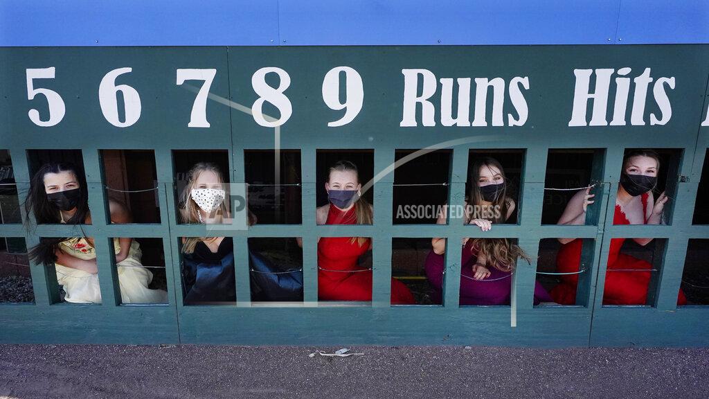 Charles Krupa While wearing their prom gowns, students peer through the scoreboard at the New Hampshire Fisher Cats minor league baseball stadium in Manchester, N.H., on Monday, April 26, 2021. After a year without proms, school districts across the country are debating whether they can safely hold an event that many seniors consider a capstone to their high school experience. The nearly 300 student senior class of Manchester's Central High School are waiting to get approval from the city's board of health so they can have their prom at the outdoor venue, due to COVID-19 concerns. (AP Photo/Charles Krupa)