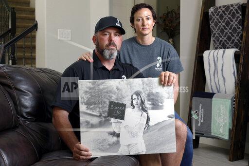 In this Oct. 12, 2021, photo, David and Wendy Mills, parents of Kailee Mills who was killed four years ago in an automobile accident when riding in the back seat without a seat belt, with a photo of their daughter at their home in Spring, Texas. The teenager was riding in the back seat of a car to a Halloween party in 2017 just a mile from her house when she unfastened her seat belt to slide next to her friend and take a selfie. Moments later, the driver veered off the road and the car flipped, ejecting her. (AP Photo/Michael Wyke)