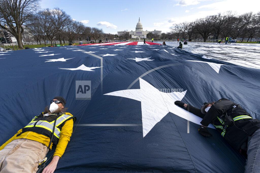 Alex Brandon Workers use their body weight to hold down a large American flag placed on the National Mall, with the U.S. Capitol behind them, ahead of the inauguration of President-elect Joe Biden and Vice President-elect Kamala Harris, Monday, Jan. 18, 2021, in Washington. (AP Photo/Alex Brandon)