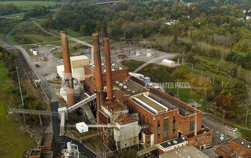 CORRECTS SPELLING OF GREENIDGE - Smokestacks from the Greenidge Generation power plant tower above nearby homes, Friday, Oct. 15, 2021, in Dresden, N.Y. One Bitcoin mining operation in central New York came up with a novel solution in finding cheap energy to run the power-gobbling computer arrays that create and transact cryptocurrency: It took over Greenidge Generation which now produces about 44 megawatts to run 15,300 computer servers, plus additional electricity it sends into the state's power grid. (AP Photo/Julie Jacobson)